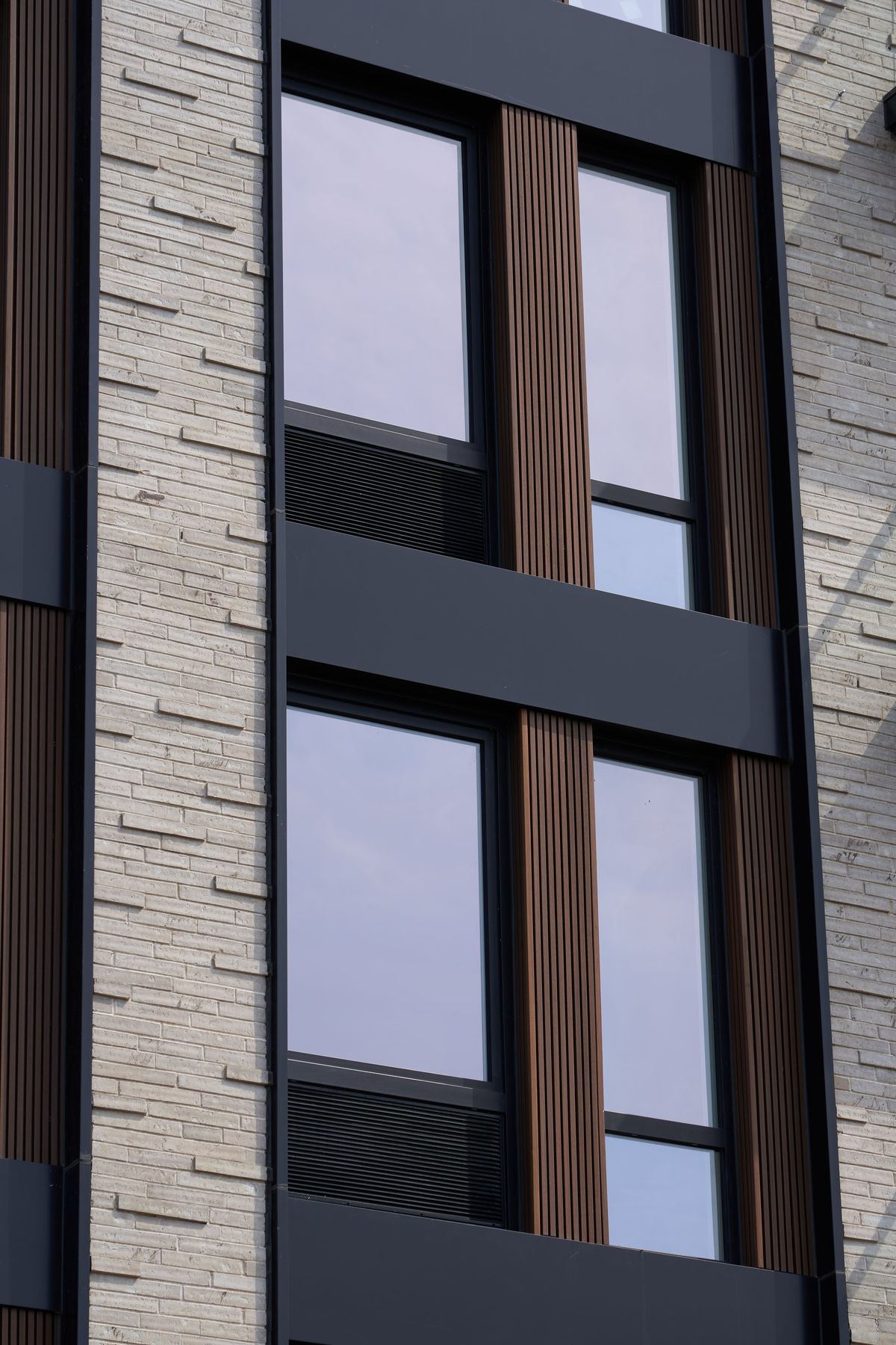 A black window from outside: a fixed lite over a louver band in the same frame, a narrow lite beside it, between wood-look slats